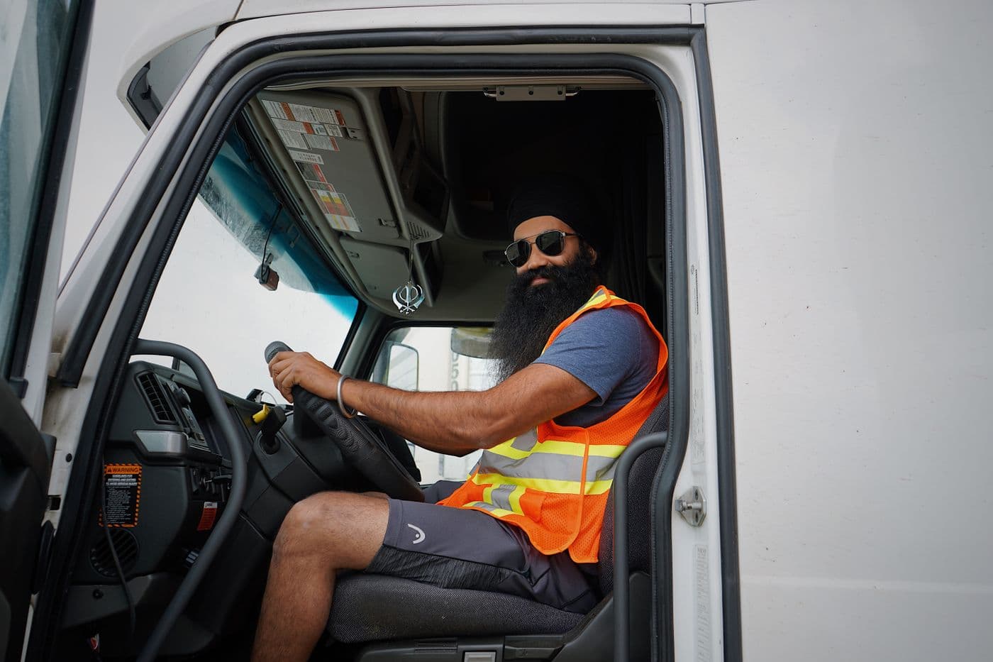 A professional CDL-A truck driver in the cab, wearing a safety vest
